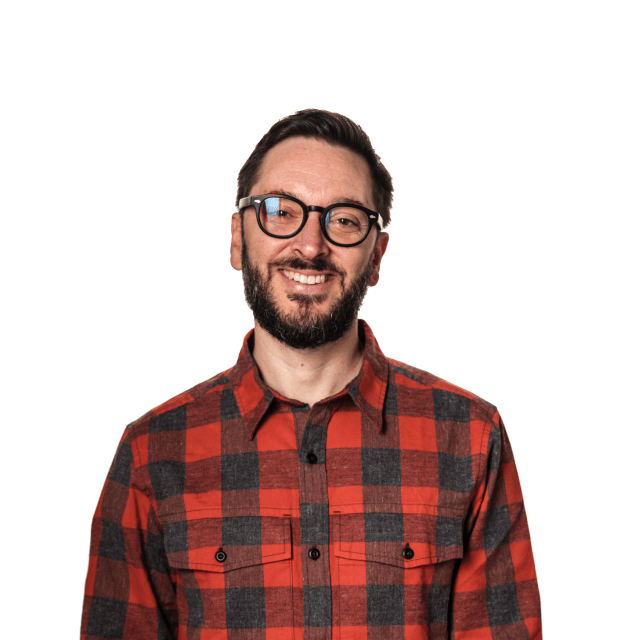 Smiling man in a red and black plaid shirt, representing community engagement at the Love Bomb 2015 event supporting Street Roots.